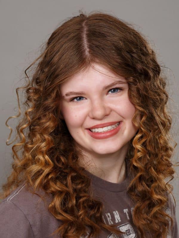 Jones-family-orthodontics-nora Young girl smiling with curly hair and purple shirt at jones family orthodontics
